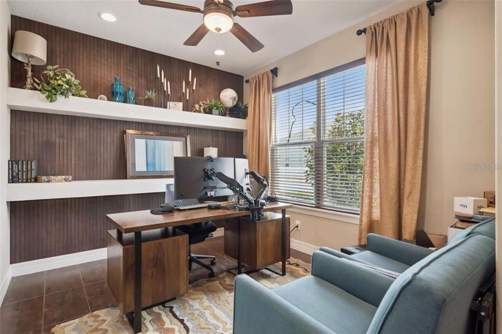 A home office features a wooden desk, dual monitors, floating shelves, and two blue chairs — 2683 AMATI DRIVE, KISSIMMEE, FL