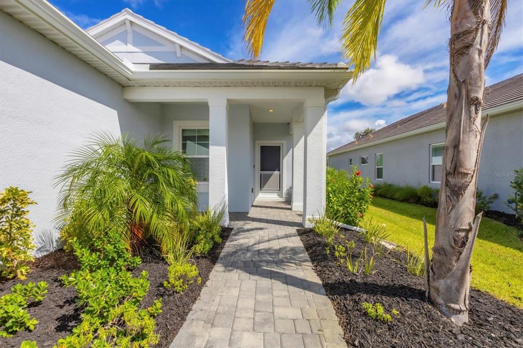A paved walkway leads to the covered front entrance of a light-colored stucco house — 12760 BROOKGREEN STREET, VENICE, FL