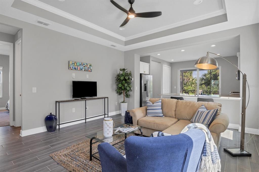 A living room features a beige sectional, blue armchair, dark wood-look tile flooring, and ceiling fan — 12760 BROOKGREEN STREET, VENICE, FL