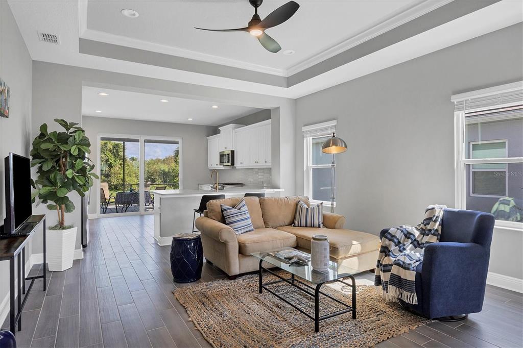 A living room with a tan sectional, blue armchair, and kitchen in the background — 12760 BROOKGREEN STREET, VENICE, FL