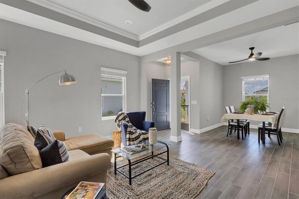 An open-concept living and dining area features gray walls, wood-look tile flooring, and tray ceilings — 12760 BROOKGREEN STREET, VENICE, FL
