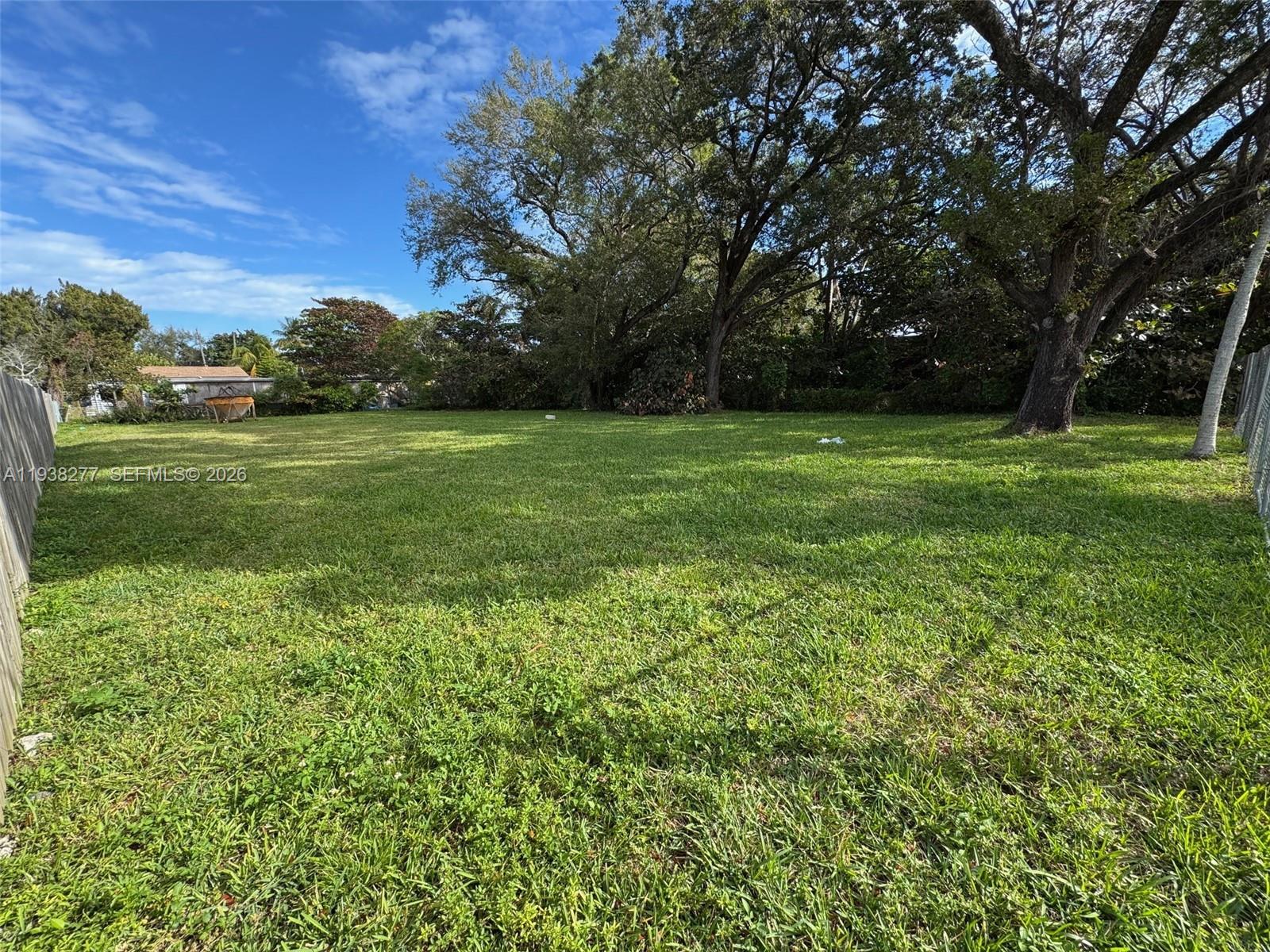 A large, grassy backyard features mature trees and a wooden fence along the side — 261 NW 96th St, Miami FL 33150, MIAMI, FL