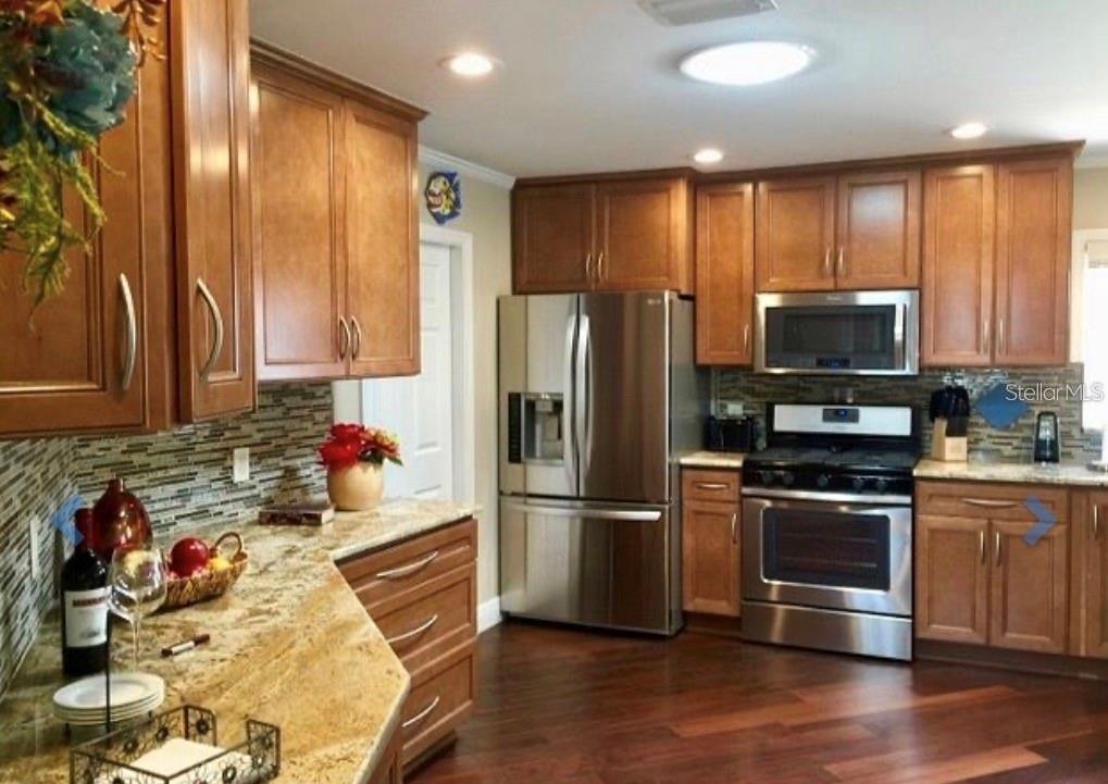 A kitchen with wood cabinets, stainless steel appliances, granite countertops, and a tile backsplash — 1041 REIDVILLE ROAD, THE VILLAGES, FL