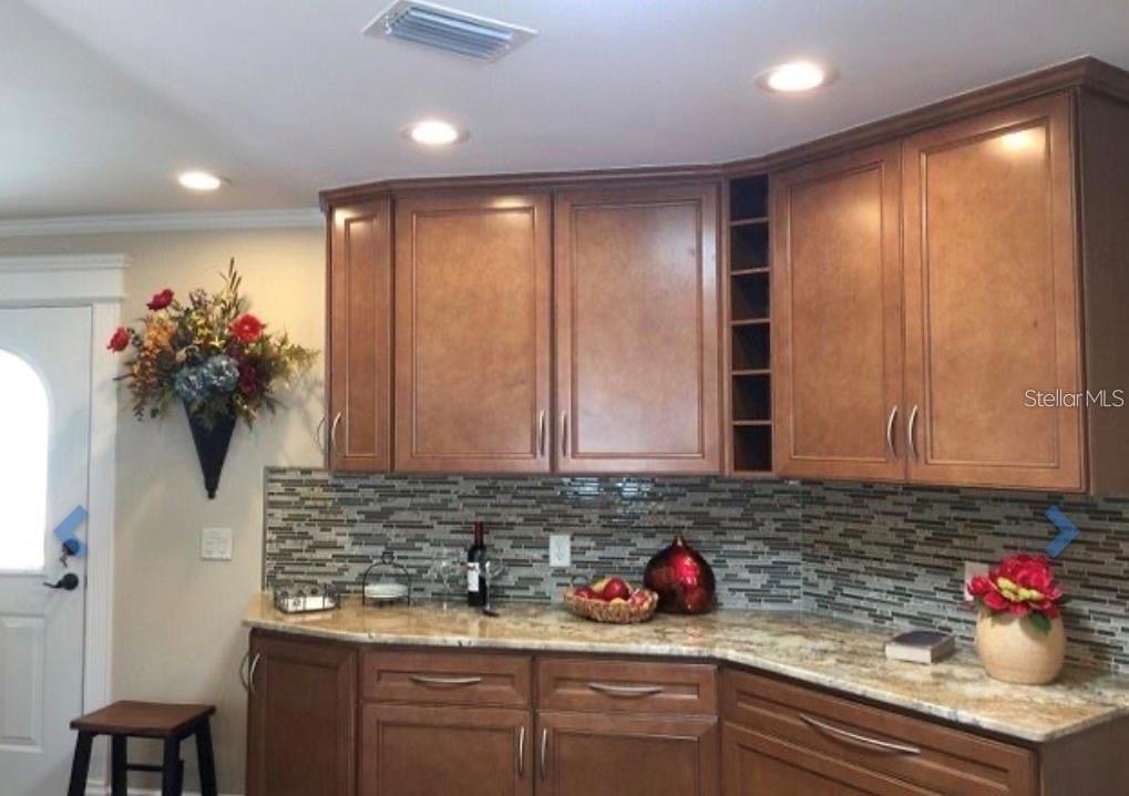 A kitchen area features wood cabinets, granite countertops, and a decorative tile backsplash — 1041 REIDVILLE ROAD, THE VILLAGES, FL