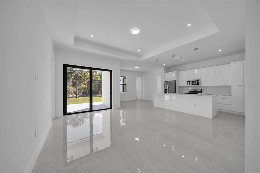 A modern, open-concept kitchen and living area with white cabinetry, tile flooring, and sliding doors — 4703 SARA AVE N, LEHIGH ACRES, FL