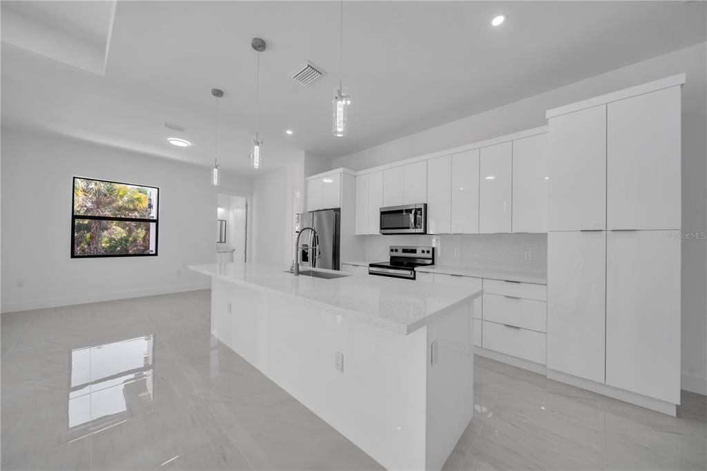 A modern kitchen features white cabinetry, a large island with a sink, and tile flooring — 4703 SARA AVE N, LEHIGH ACRES, FL