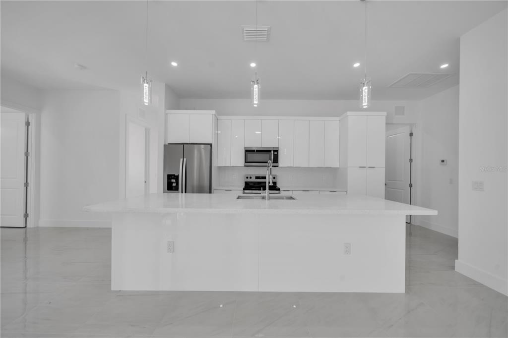 A modern kitchen features white cabinetry, a large central island, and stainless steel appliances — 4703 SARA AVE N, LEHIGH ACRES, FL