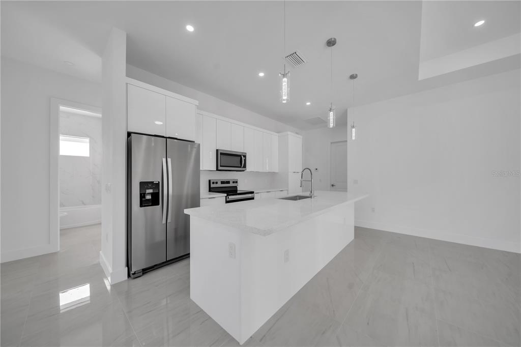 A modern kitchen features white cabinetry, stainless steel appliances, and a large central island — 4703 SARA AVE N, LEHIGH ACRES, FL