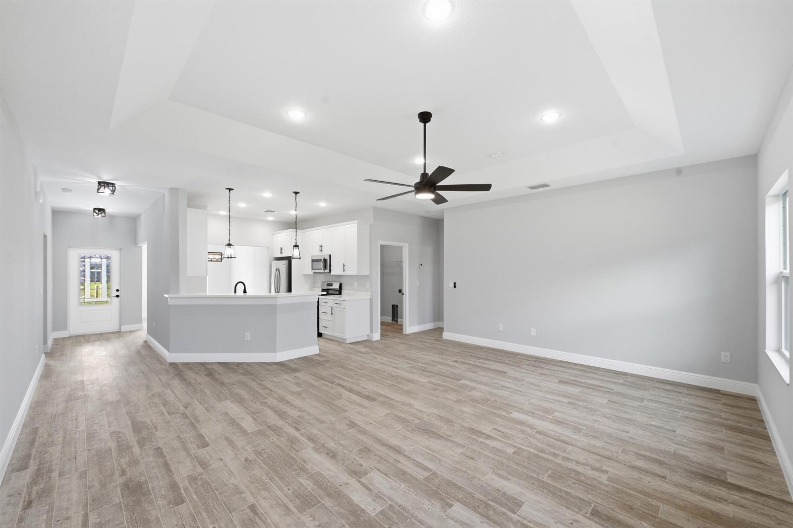An open-concept living area features light gray walls, wood-look tile flooring, and a white kitchen — 8345 100th Avenue, Vero Beach FL 32967, VERO BEACH, FL