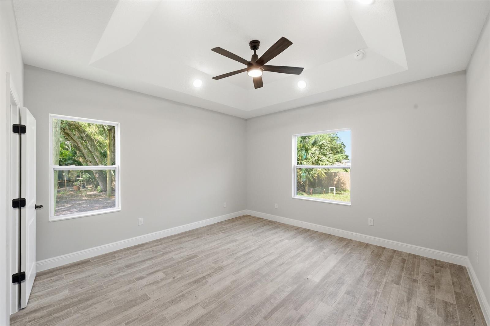 An empty bedroom features light gray walls, wood-look flooring, a tray ceiling, and a ceiling fan — 8345 100th Avenue, Vero Beach FL 32967, VERO BEACH, FL