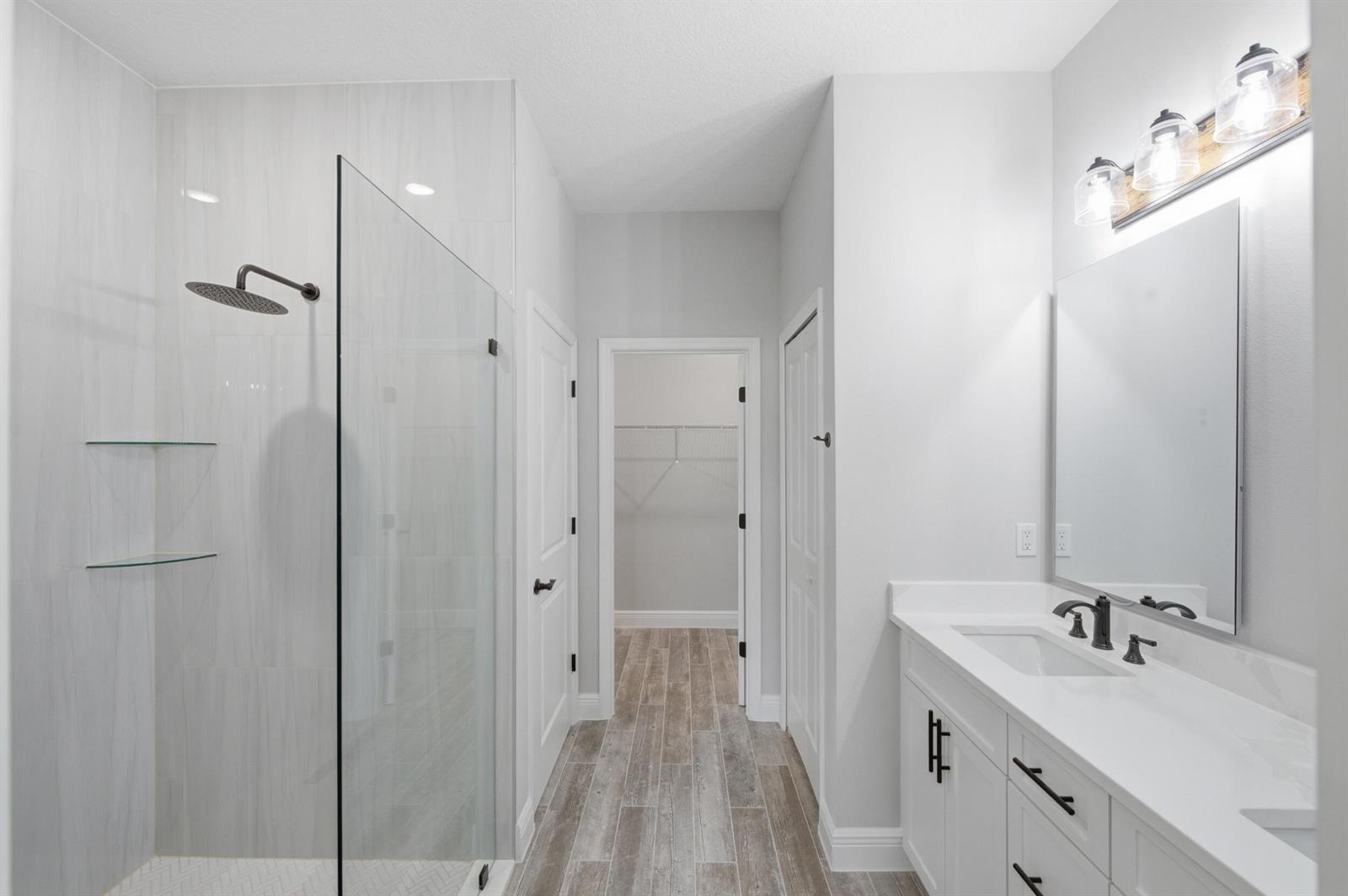 A modern bathroom features a glass-enclosed shower, a white vanity, and light wood-look tile flooring — 8345 100th Avenue, Vero Beach FL 32967, VERO BEACH, FL