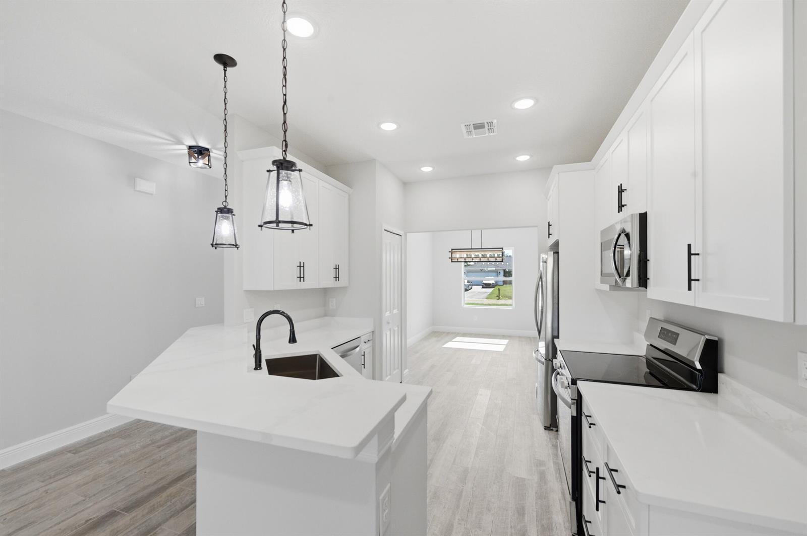 A modern kitchen features white cabinets, quartz countertops, stainless steel appliances, and light wood flooring — 8345 100th Avenue, Vero Beach FL 32967, VERO BEACH, FL