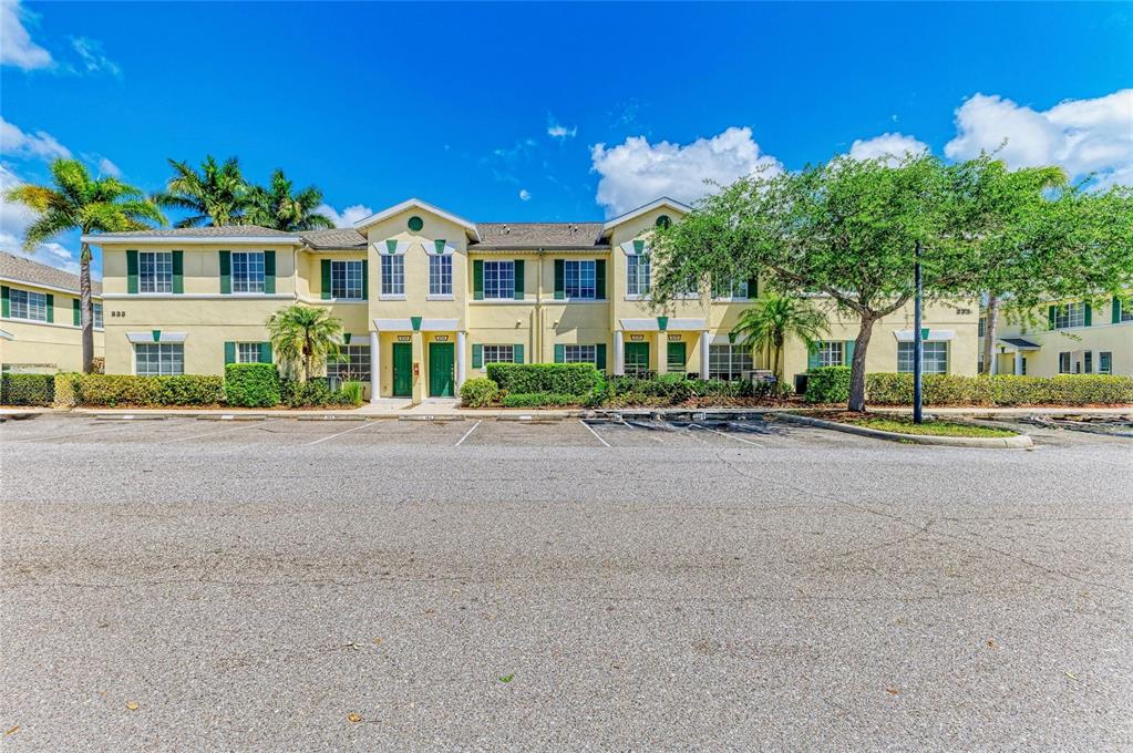A two-story yellow apartment building with green shutters stands behind a paved parking lot — 233 CAPE HARBOUR LOOP UNIT 103, BRADENTON, FL