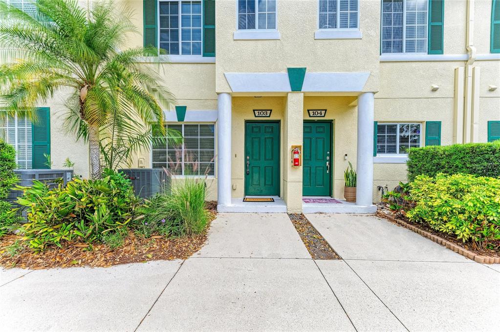 The exterior of a two-story building features two green front doors labeled 103 and 104 — 233 CAPE HARBOUR LOOP UNIT 103, BRADENTON, FL