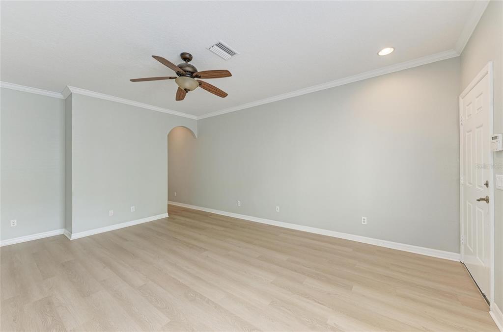 An empty living room with light-colored walls, wood-look flooring, a ceiling fan, and an arched doorway — 233 CAPE HARBOUR LOOP UNIT 103, BRADENTON, FL