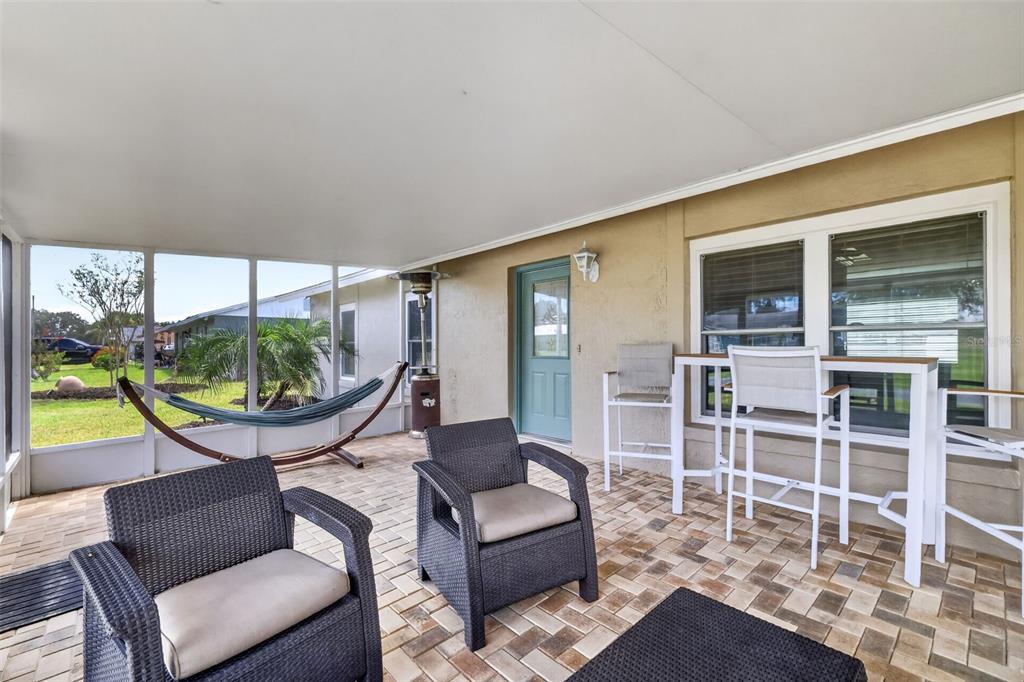 A covered patio features wicker chairs, a hammock, and a high-top table on brick pavers — 1233 PADGETT CIRCLE, LADY LAKE, FL