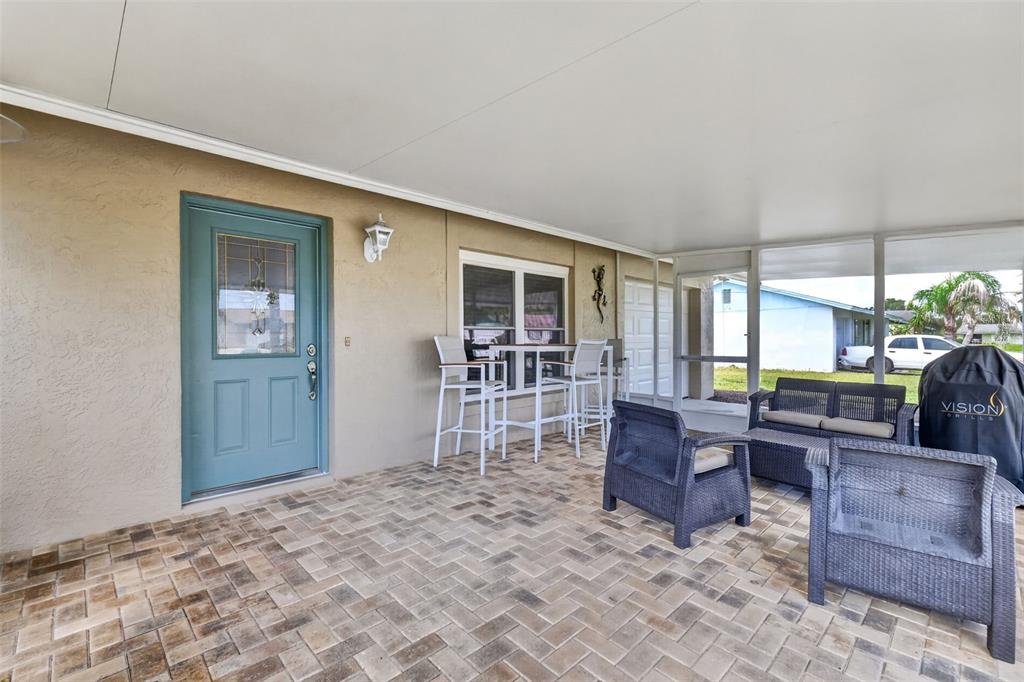 A covered patio features a teal door, paver flooring, and outdoor furniture — 1233 PADGETT CIRCLE, LADY LAKE, FL