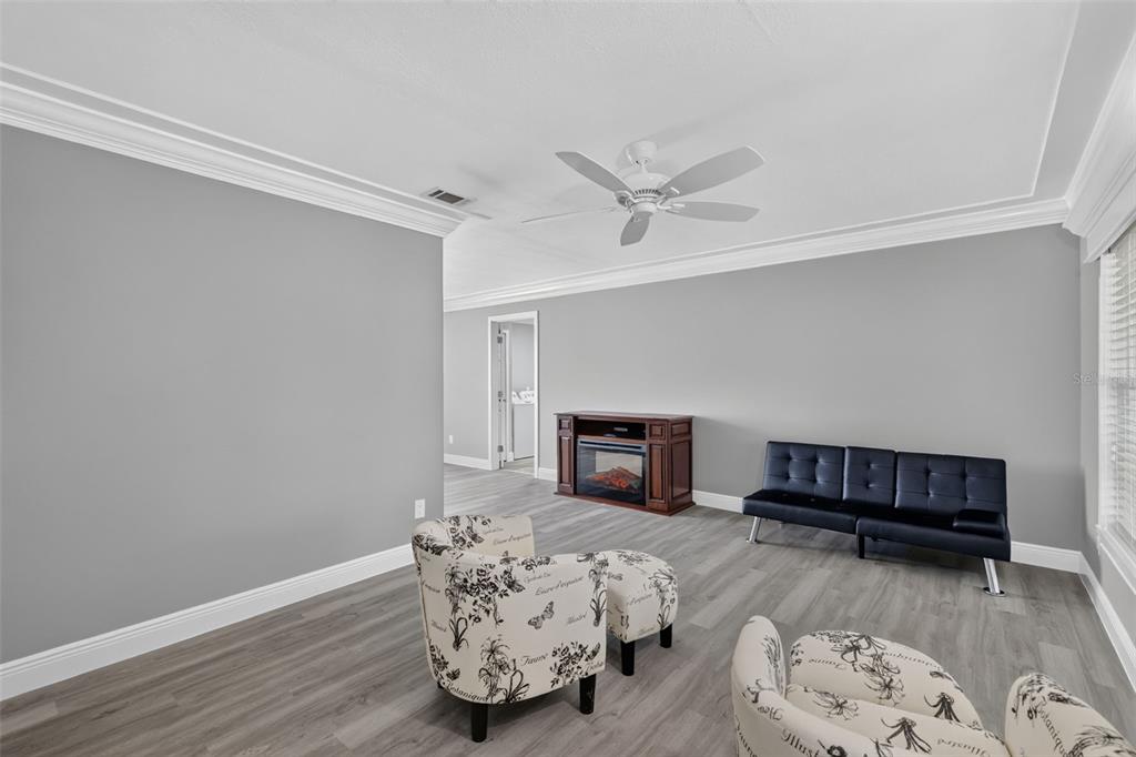 A living room features gray walls, wood-look flooring, a ceiling fan, and a small electric fireplace — 1233 PADGETT CIRCLE, LADY LAKE, FL
