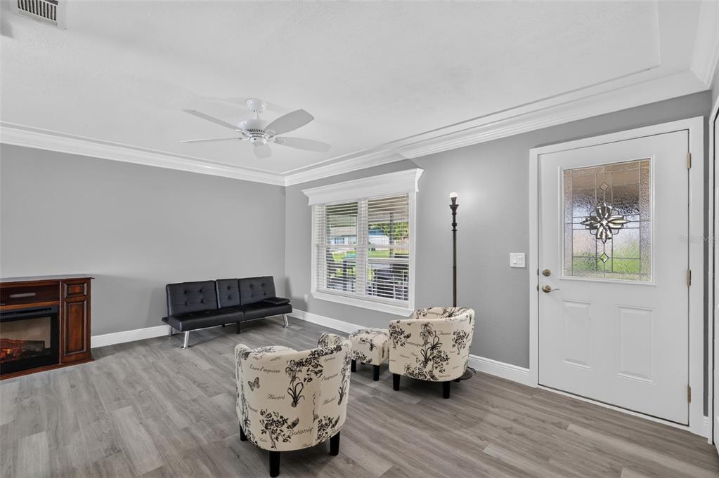 A living room features gray walls, wood-look flooring, a fireplace, a ceiling fan, and a door — 1233 PADGETT CIRCLE, LADY LAKE, FL