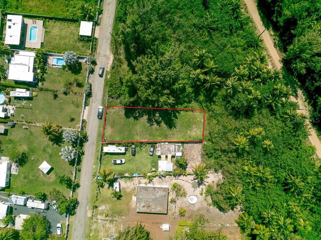 An aerial view shows a rectangular vacant lot outlined in red next to a paved road — PR 968 Km. 2.0, LAS PICUA PR 968 KM. 2.0, LOT 18A, PUNTA ARENA, LAS PICUAS UNIT 18A, RIO GRANDE, PR