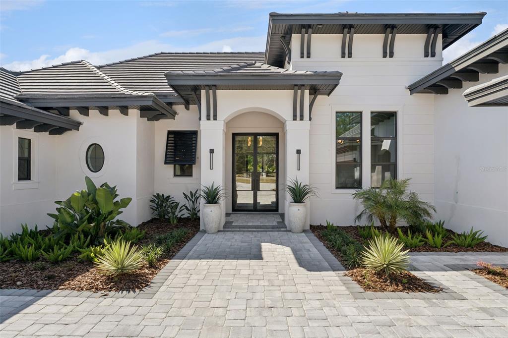 The exterior of a modern house features white stucco walls, dark trim, and a paved walkway — 16989 LUCCA LANE, MONTVERDE, FL