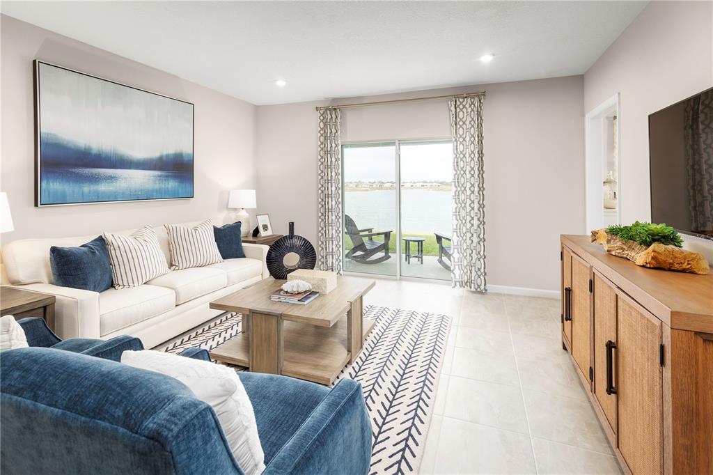 A living room features a sofa, blue armchair, coffee table, and sliding doors overlooking a lake — 1258 TURTLE ISLAND ROAD, LADY LAKE, FL