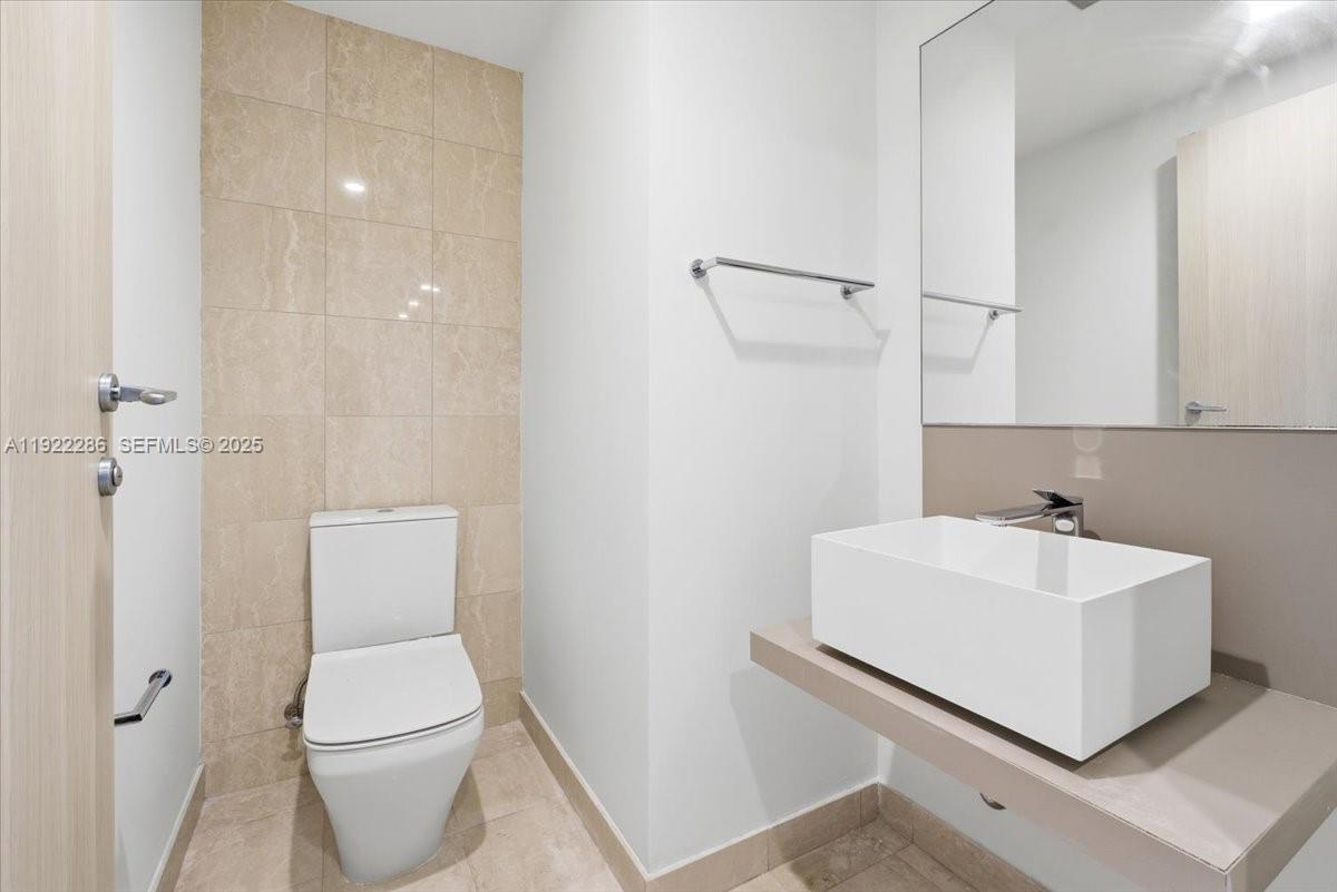 This modern half bathroom features a vessel sink, a wall-mounted mirror, and beige tiling — 1000 Brickell Plz # 3211, Miami FL 33131, MIAMI, FL