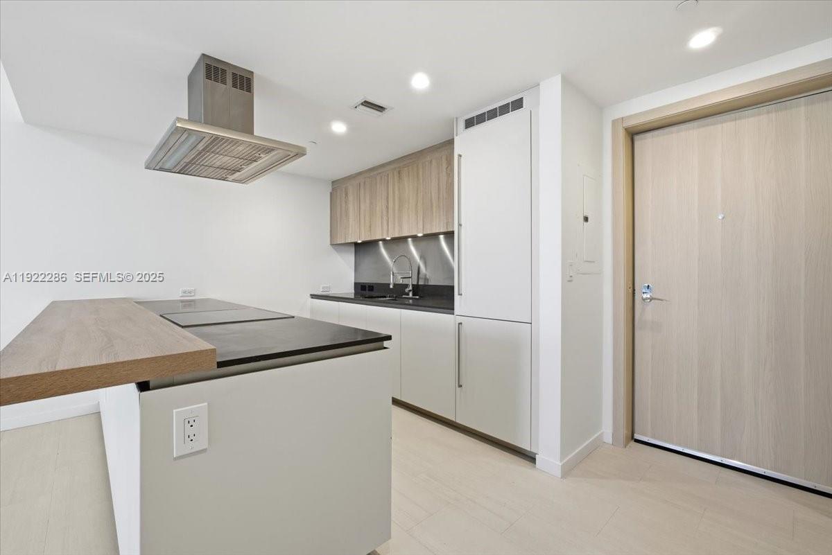 A modern kitchen features light wood cabinets, dark countertops, and a stainless steel range hood — 1000 Brickell Plz # 3211, Miami FL 33131, MIAMI, FL