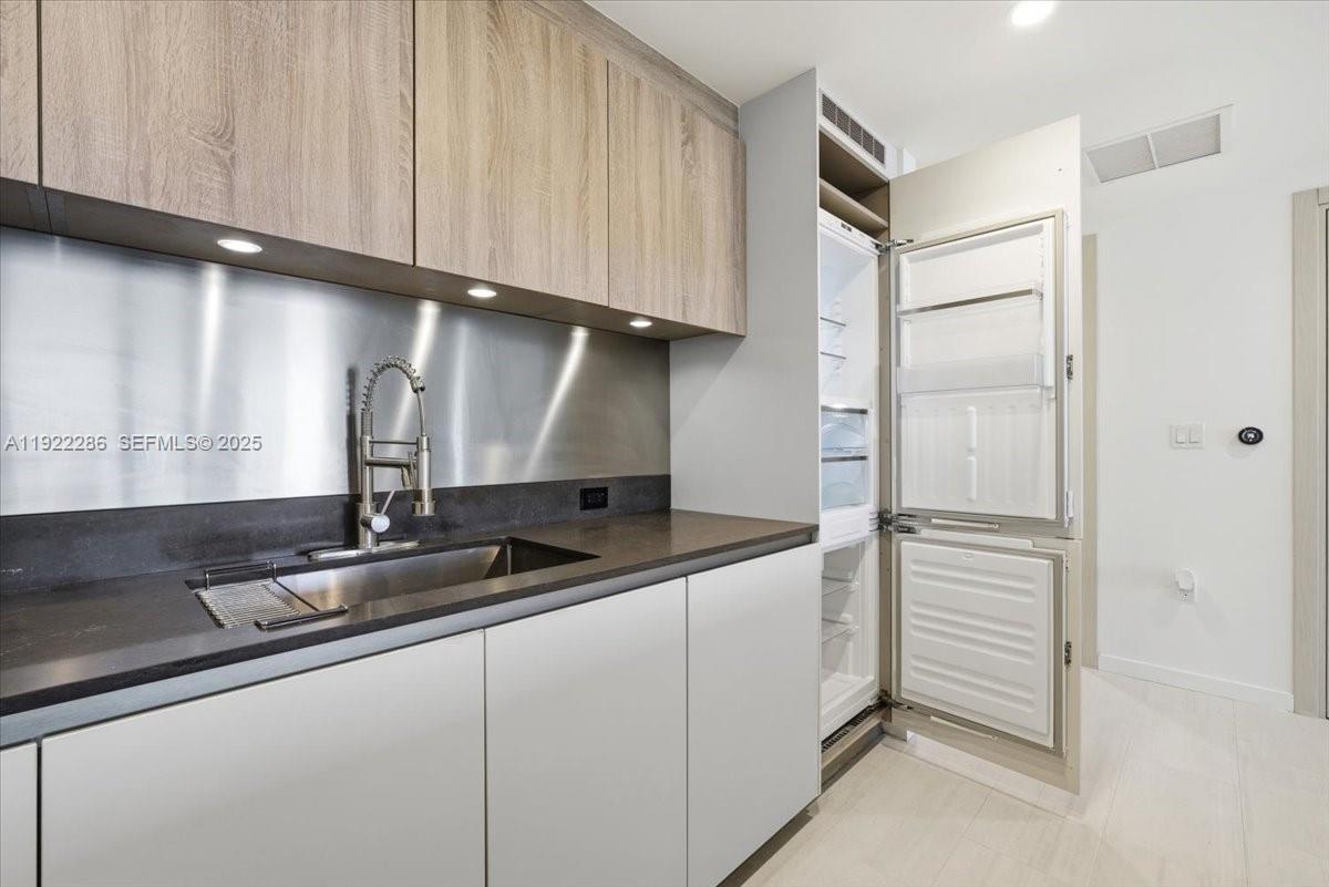 A modern kitchen features light wood cabinets, a stainless steel backsplash, and a built-in refrigerator — 1000 Brickell Plz # 3211, Miami FL 33131, MIAMI, FL