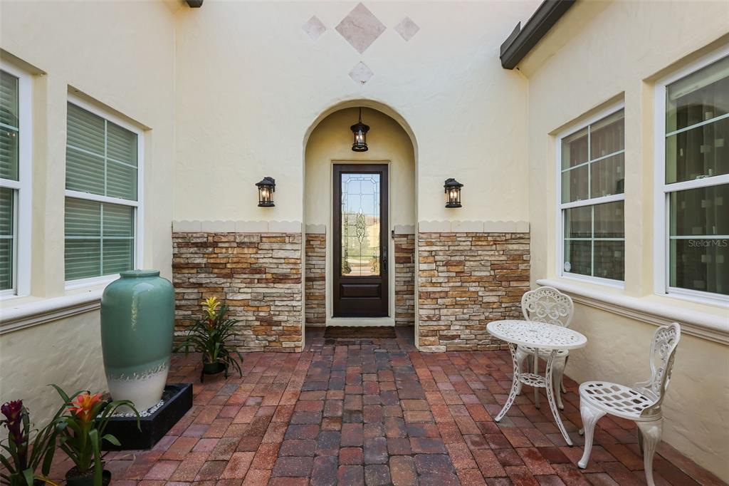 A brick-paved courtyard features a front door with an arched entryway and stone accents — 12417 MONTALCINO CIRCLE, WINDERMERE, FL
