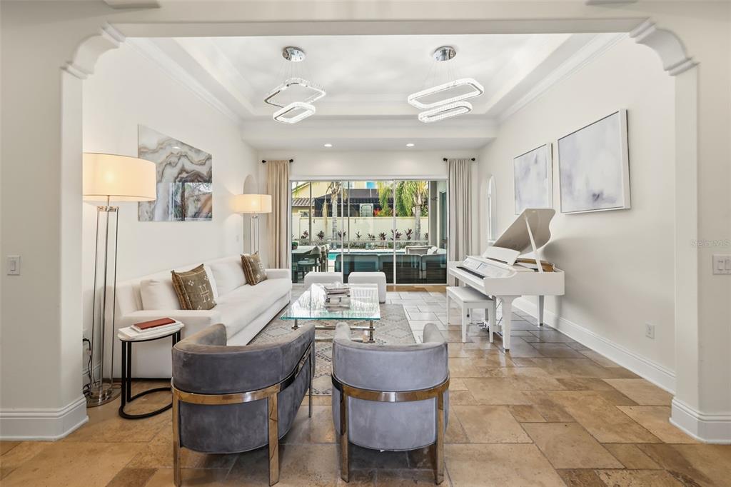 A bright living room features a white piano, modern chandeliers, and sliding glass patio doors — 12417 MONTALCINO CIRCLE, WINDERMERE, FL