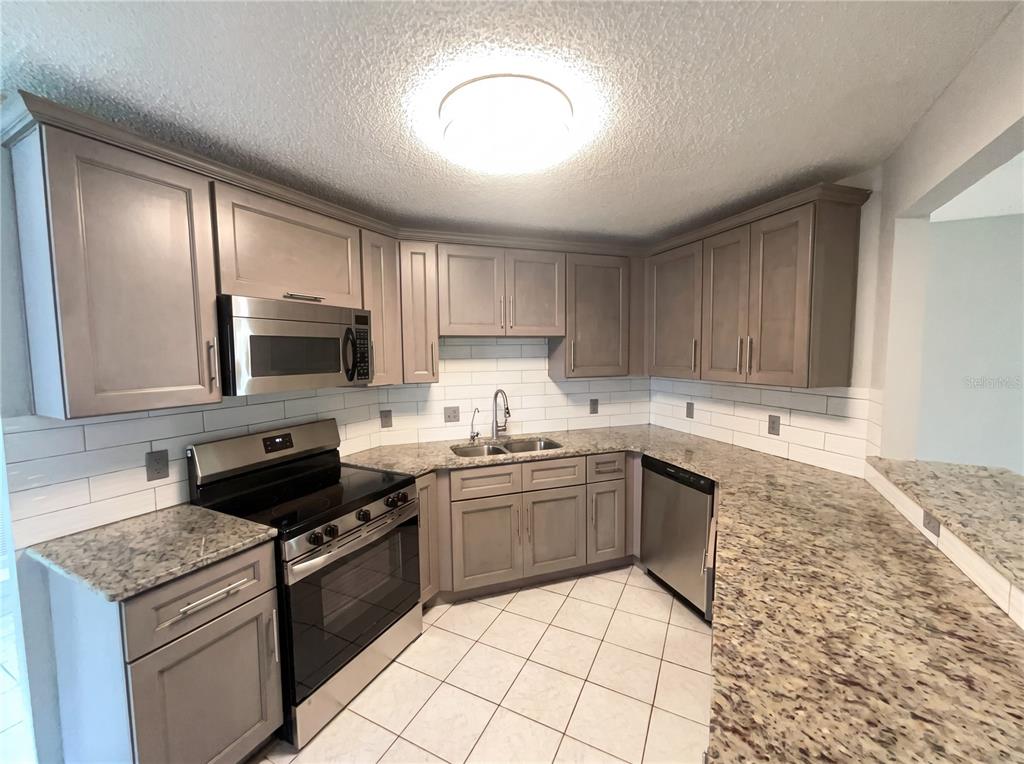 A kitchen features grey cabinets, granite countertops, stainless steel appliances, and white subway tile backsplash — 724 HARLAND COURT, KISSIMMEE, FL
