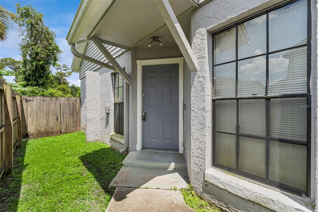 A gray front door sits under a small porch overhang next to a large window — 533 MADRIGAL COURT, ORLANDO, FL