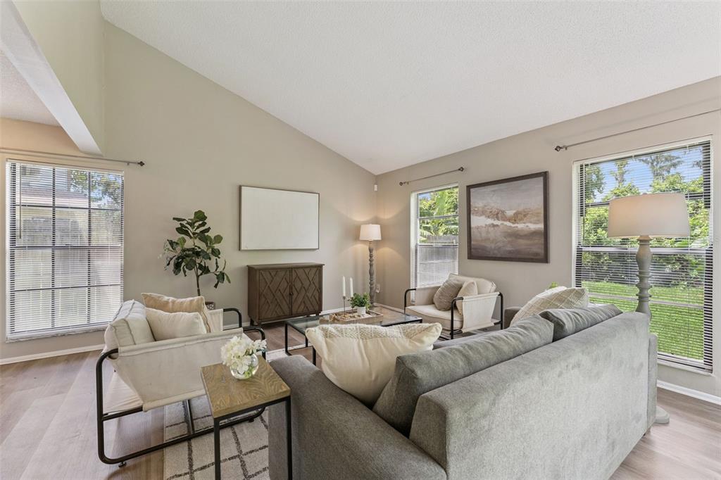 A living room with a vaulted ceiling, gray sofa, two armchairs, and large windows — 533 MADRIGAL COURT, ORLANDO, FL