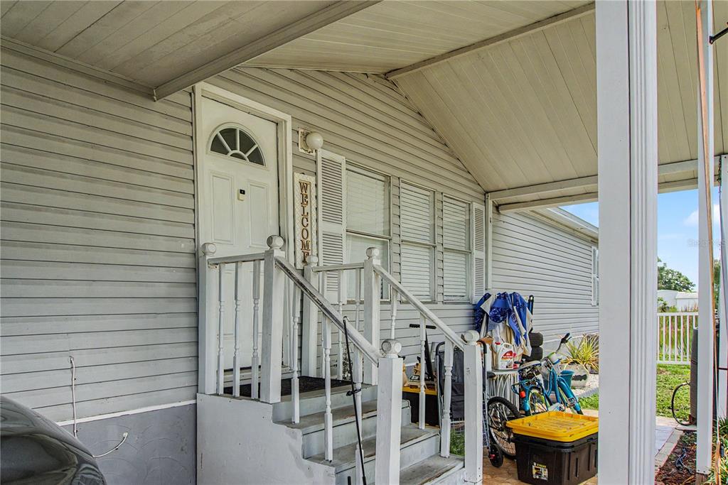 A covered porch with white siding, a front door, and wooden stairs leading to the entrance — 6601 51ST WAY N, PINELLAS PARK, FL