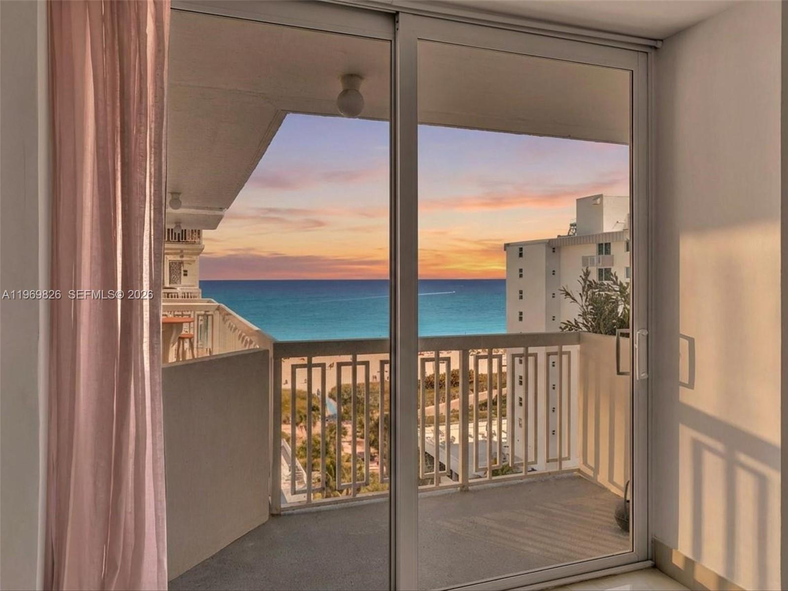 A view of the ocean and sunset from a balcony through sliding glass doors — 401 Ocean Dr # 1007, Miami Beach FL 33139, MIAMI BEACH, FL