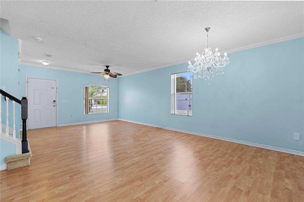 An empty living room with light blue walls, wood-look flooring, a chandelier, and a ceiling fan — 51 PINE FOREST PLACE, APOPKA, FL