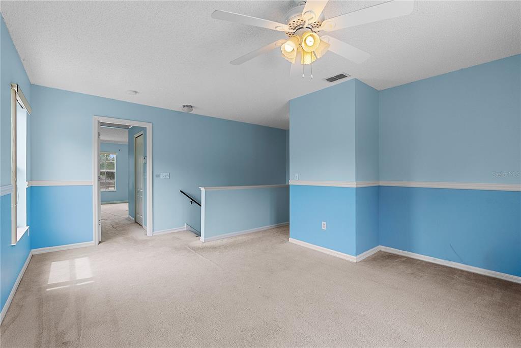 A carpeted room with light blue walls, white wainscoting, and a ceiling fan — 51 PINE FOREST PLACE, APOPKA, FL