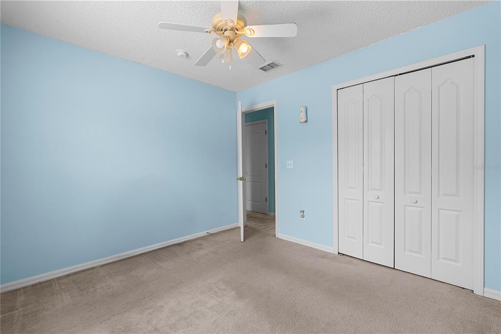 An empty bedroom with light blue walls, beige carpet, a ceiling fan, and white closet doors — 51 PINE FOREST PLACE, APOPKA, FL