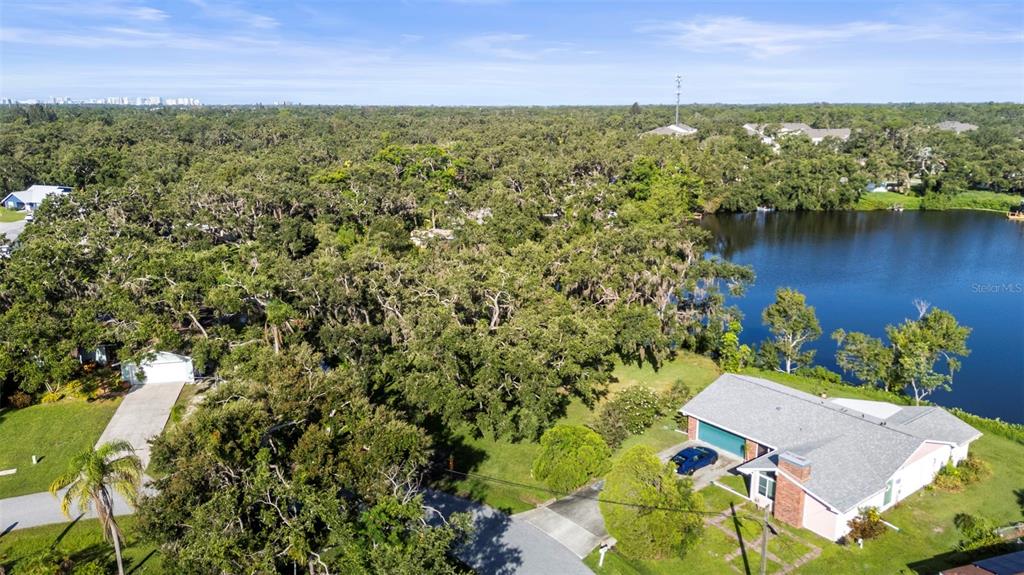 An aerial view shows a house with a gray roof next to a lake and trees — 5405 SAN JUAN DRIVE, SARASOTA, FL