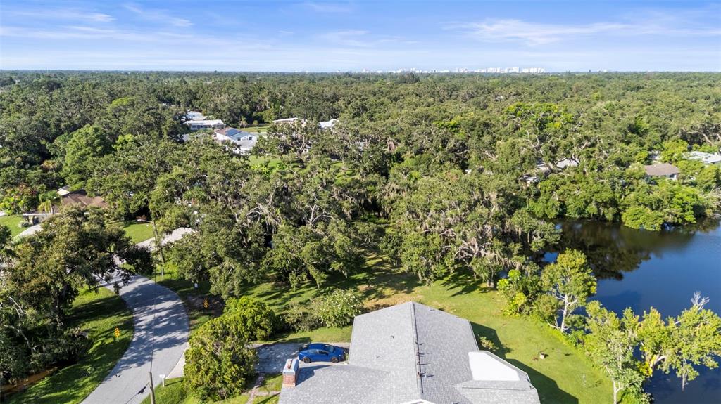An aerial view shows a house with a gray roof next to a lake and trees — 5405 SAN JUAN DRIVE, SARASOTA, FL