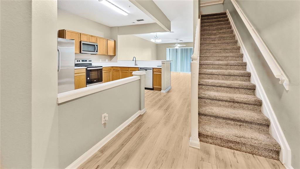 A kitchen with wood cabinets and stainless steel appliances sits beside a carpeted staircase — 6292 TWAIN STREET UNIT 102, ORLANDO, FL