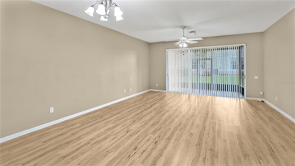 An empty living room features light wood-look flooring, beige walls, a ceiling fan, and vertical blinds — 6292 TWAIN STREET UNIT 102, ORLANDO, FL