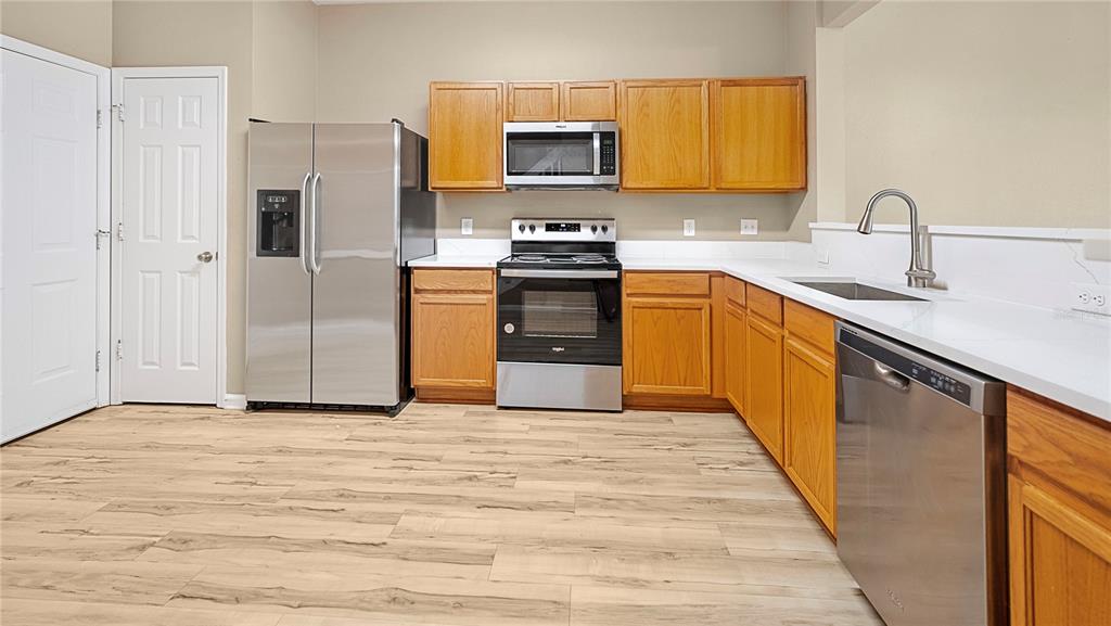 A kitchen with wood cabinets, stainless steel appliances, white countertops, and light wood-look flooring — 6292 TWAIN STREET UNIT 102, ORLANDO, FL