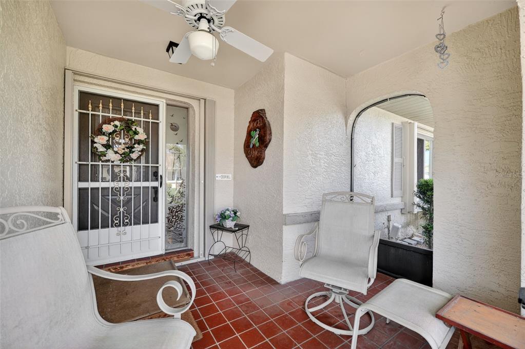 A covered porch features red tile flooring, white patio furniture, and a ceiling fan — 2322 LANCASTER DRIVE, SUN CITY CENTER, FL