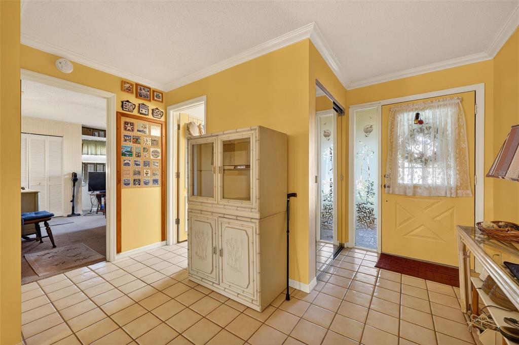 An entryway with yellow walls, tile flooring, a white cabinet, and a front door — 2322 LANCASTER DRIVE, SUN CITY CENTER, FL