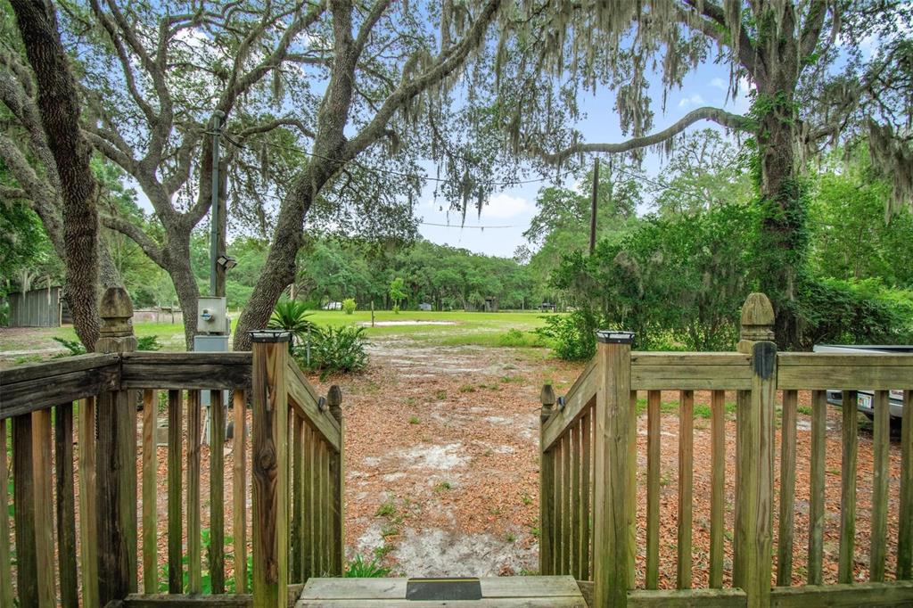 A wooden deck with railings overlooks a sandy yard shaded by large oak trees — 156 KINGFISH ROAD, POMONA PARK, FL