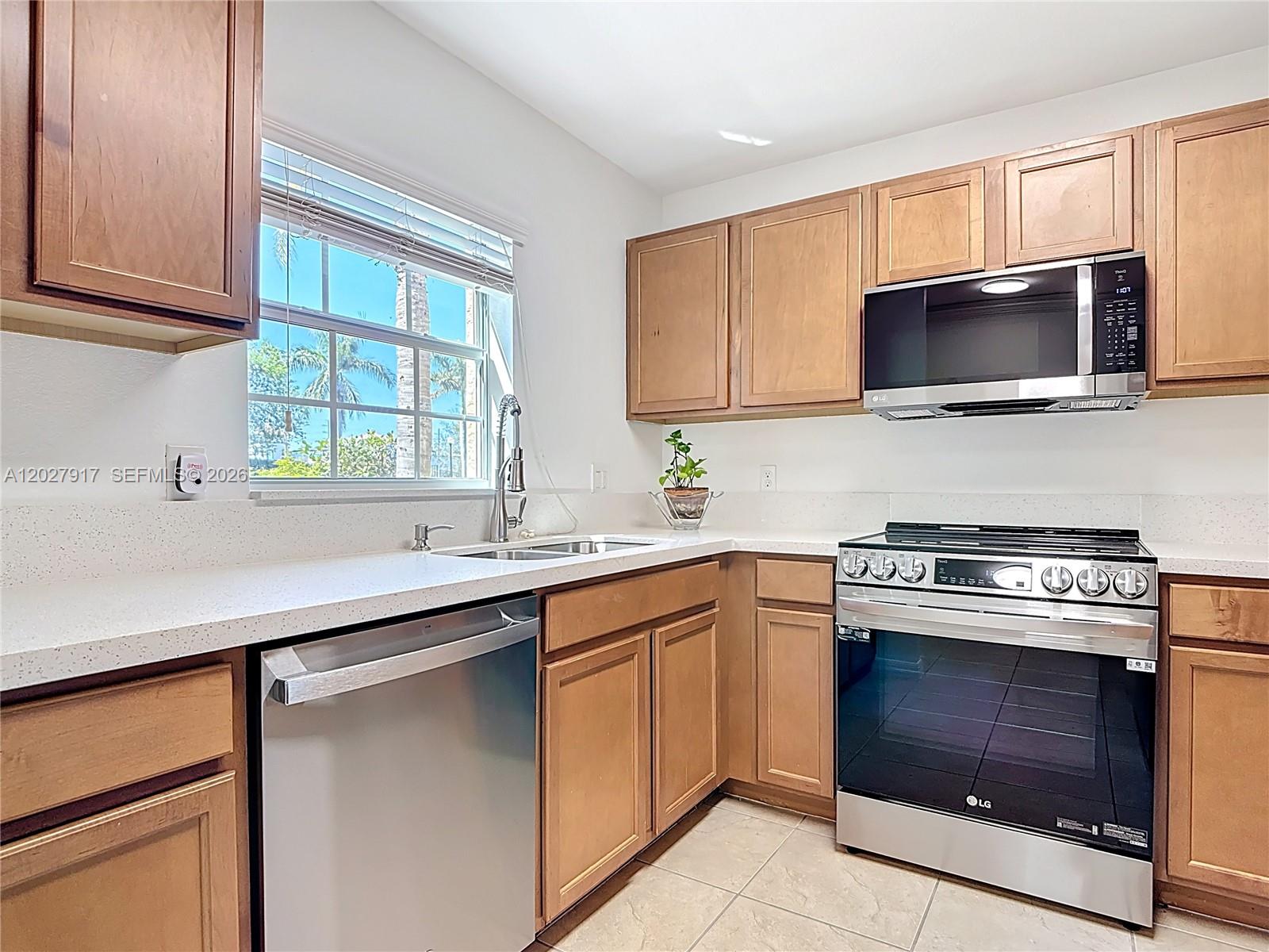 A kitchen features wood cabinets, stainless steel appliances, white countertops, and a window view — 9101 GERVAIS # 1705, Naples FL 34120, NAPLES, FL