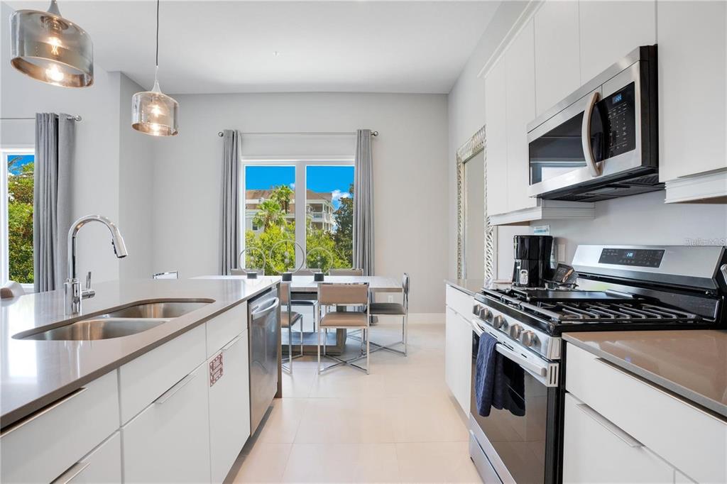 A modern kitchen features white cabinetry, stainless steel appliances, and a view of a dining area — 7760 SANDY RIDGE DRIVE UNIT 200, REUNION, FL