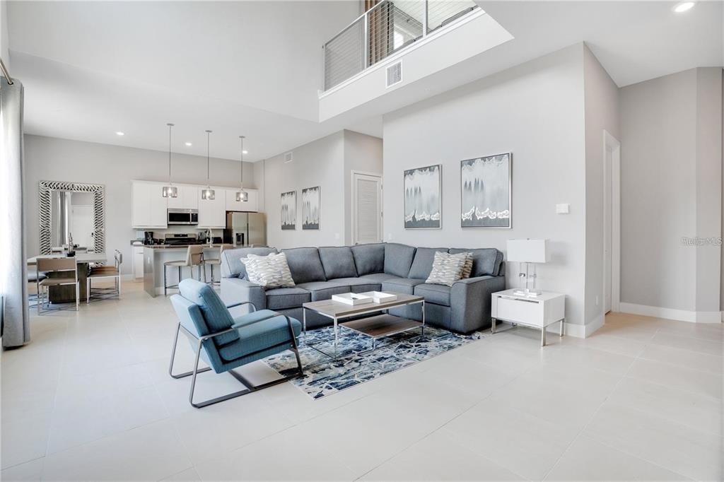A spacious open-concept living room features a grey sectional, blue armchair, and a modern kitchen — 7760 SANDY RIDGE DRIVE UNIT 200, REUNION, FL